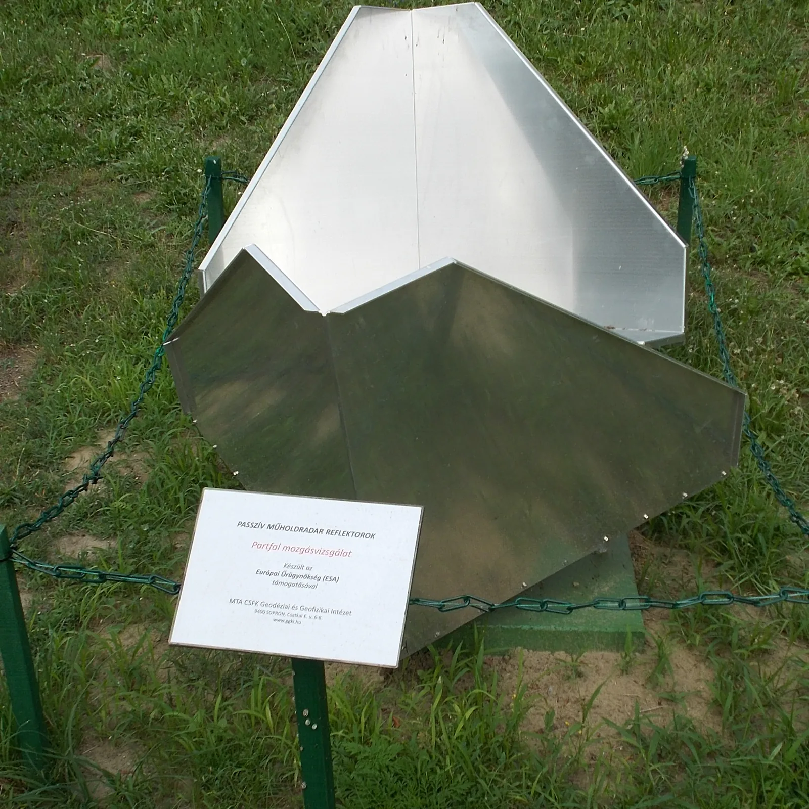 A metal corner reflector for satellite radar installed on a grassy embankment