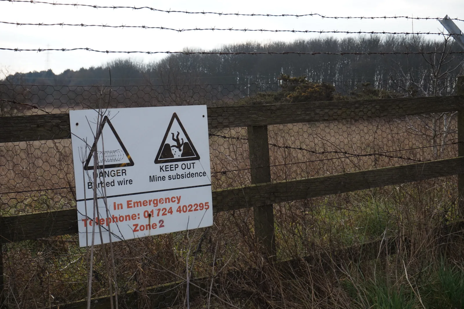 A fence with a mine subsidence warning sign in front of woodland