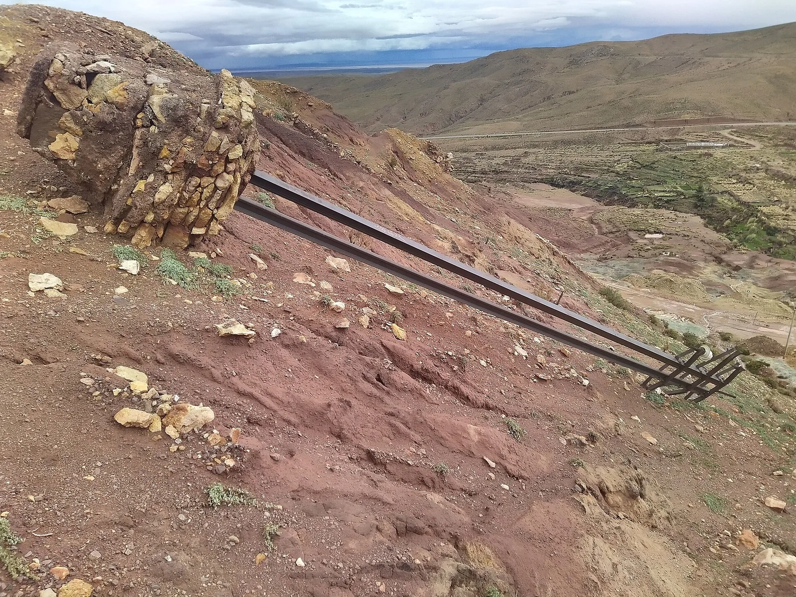 A medium-voltage pole lying on an eroded slope, pulled down with its foundation block