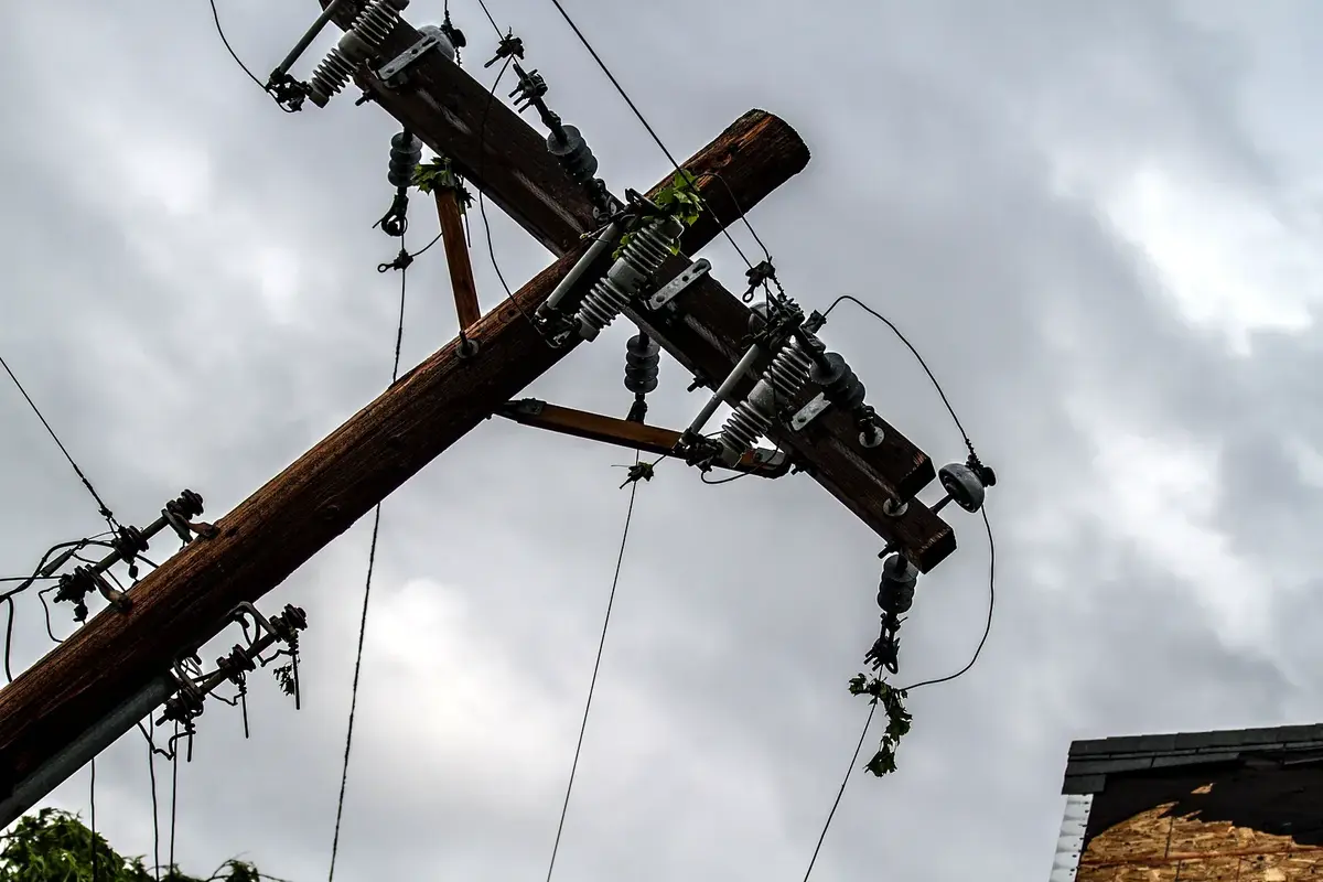 La parte superior de un poste dañada por una tormenta, con crucetas, aisladores y conductores colgando